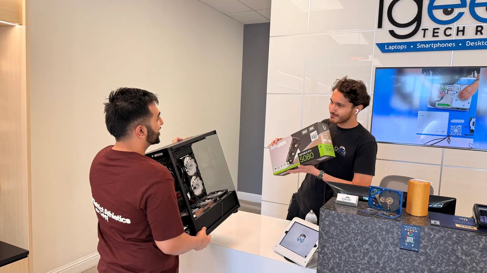 Technician showing a graphics card box beside an open custom PC at the counter